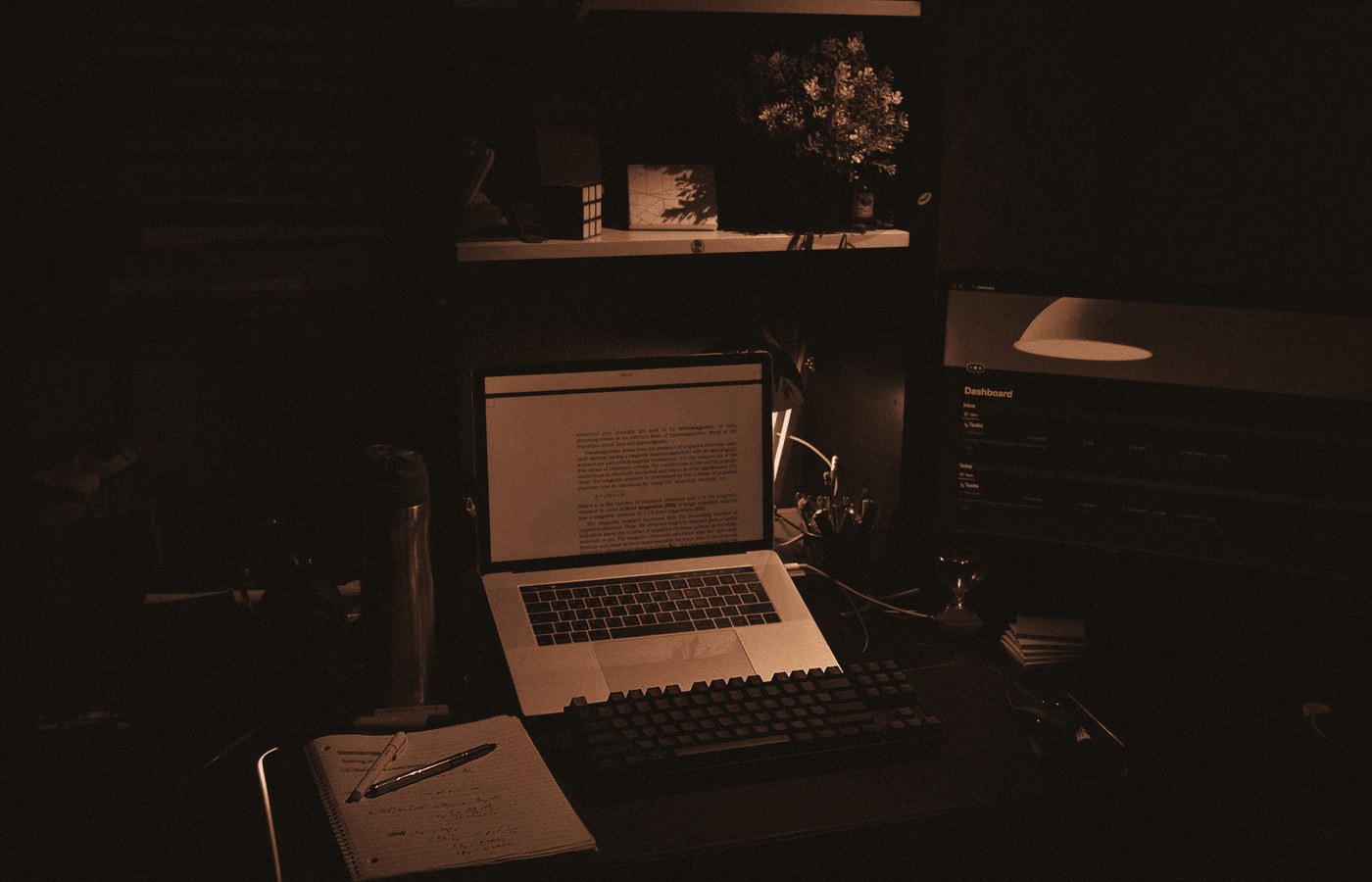 A home desk at night, laptop open, notebook and pen beside it